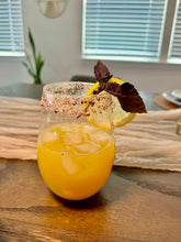 Load image into Gallery viewer, Glass rimmed with beautiful colored floral cocktail salt with orange juice and ice inside.