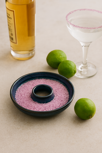 Handmade blue ceramic cocktail salt rimmer filled with pink beautyberry salt, surrounded by limes and a glass of tequila