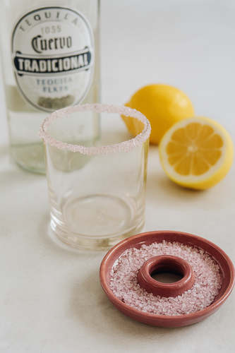 Tequila bottle, glass with salt rim, and lemons on a light surface
