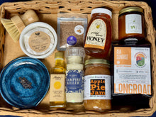 Load image into Gallery viewer, A Farmer’s Market Harvest Box filled with Jacksonville-made goods including honey, garlic salt, coffee, jam, olive oil, candle, dish soap, and a handmade blue spoon rest.
